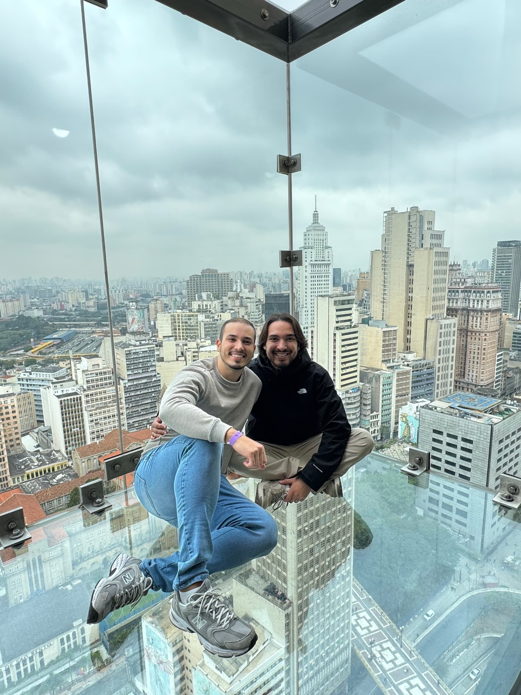 Lucas e Thiago em um mirante de vidro sobre a cidade